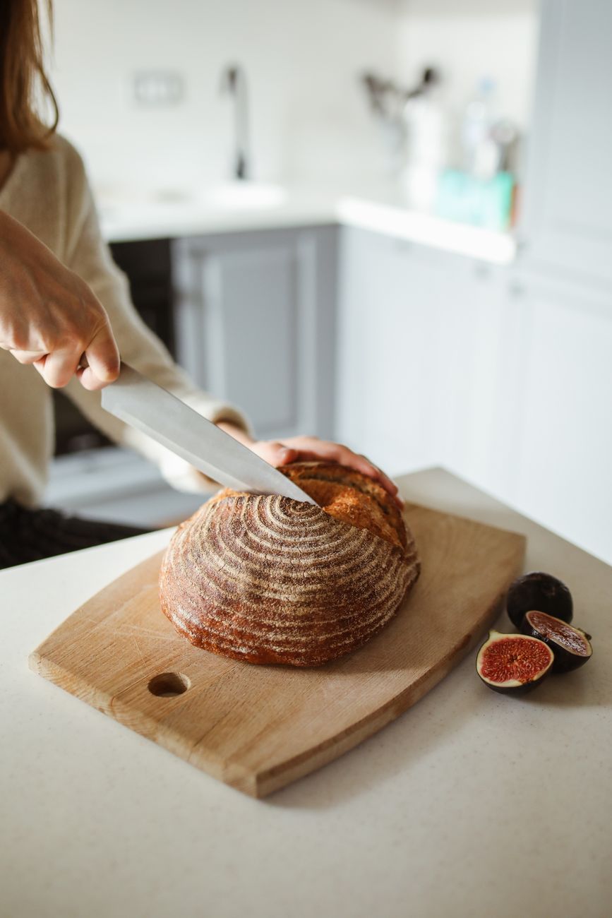 A cook slicing artisan bread on a wooden cutting board with fresh figs beside it — one good board doing dinner-party work.